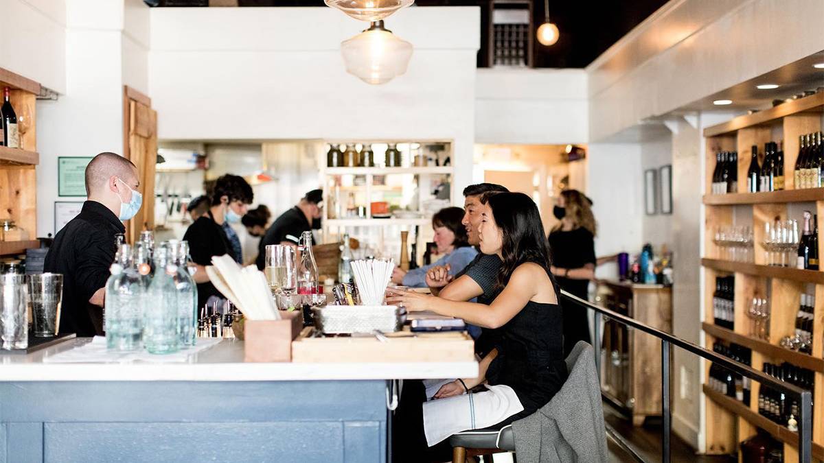 People sitting at the bar eating with a wall lined with wine bottle behind them at Eden Hill Restaurant in Seattle, Washington, USA